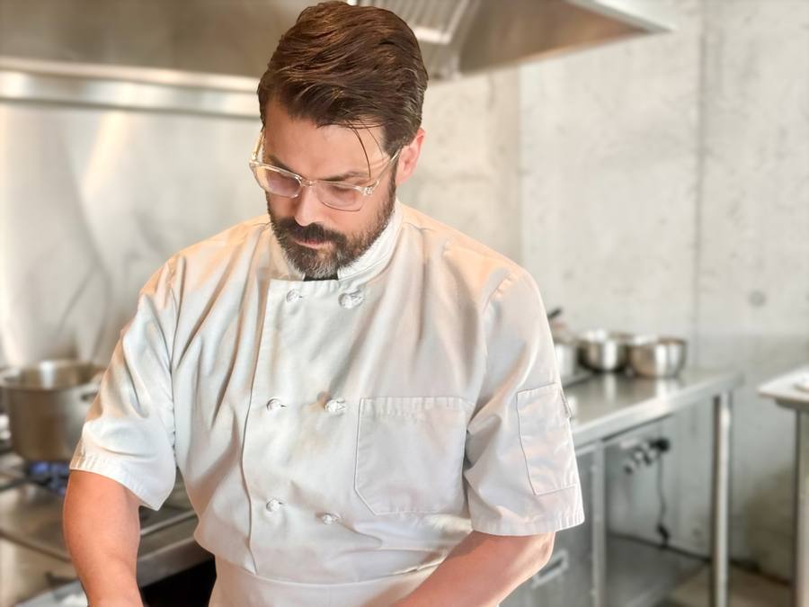 Jesse Brune in chef whites, working at the pass in a professional kitchen.
