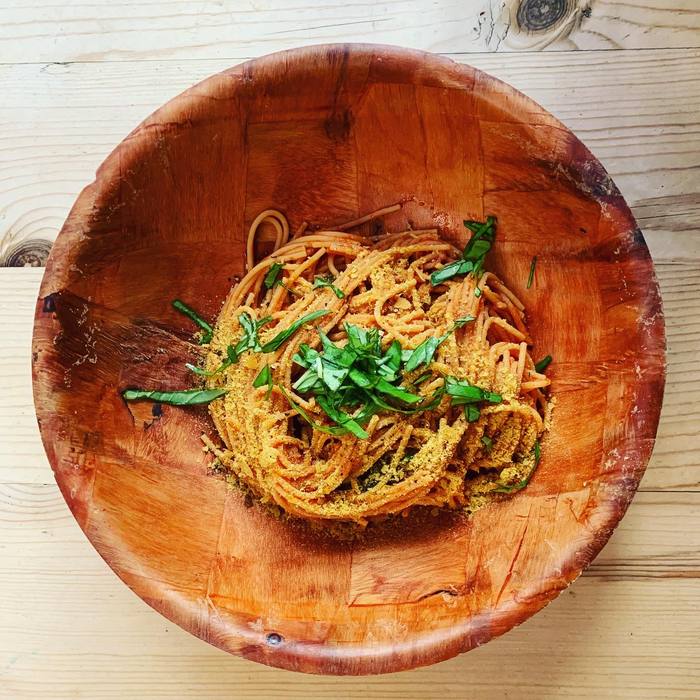 Vegan spaghetti in a wooden bowl with tomato sauce, nutritional yeast and torn basil.